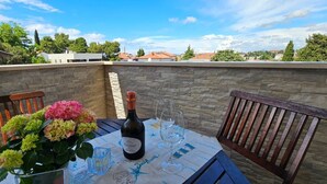 Ein Tisch mit einer Weinflasche, Gläsern und einem Blumenstrauß auf einer Terrasse mit Steinmauern und Holzstühlen.