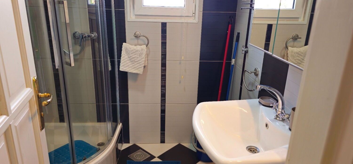 A bathroom with a glass shower enclosure, a white sink, and a blue and white tiled floor.