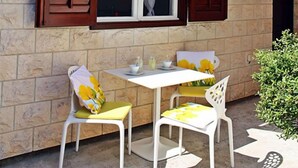 A stone building with a tiled roof, a bell tower, and a covered outdoor seating area with two chairs and a table. - House Ivi (Supetar)