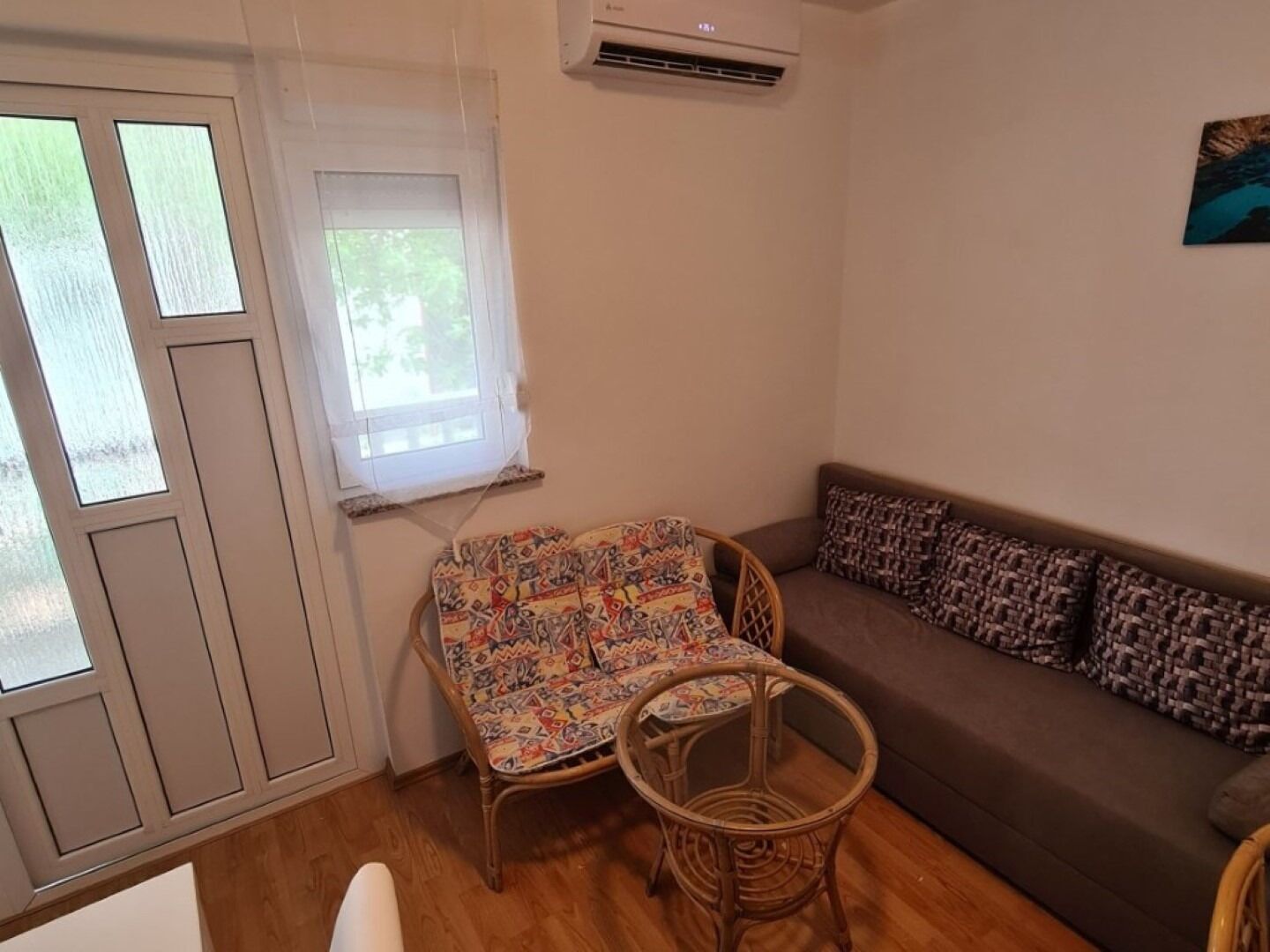 A living room with a sofa, two wicker chairs, a window, and an air conditioning unit.