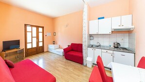 A compact living space with a kitchenette, a television, a red sofa, and a dining area. - Apartments Sunny (Makarska)