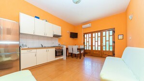 A compact kitchen with white cabinets, a stove, and a dining area with a table and chairs. - Apartments Sunny (Makarska)