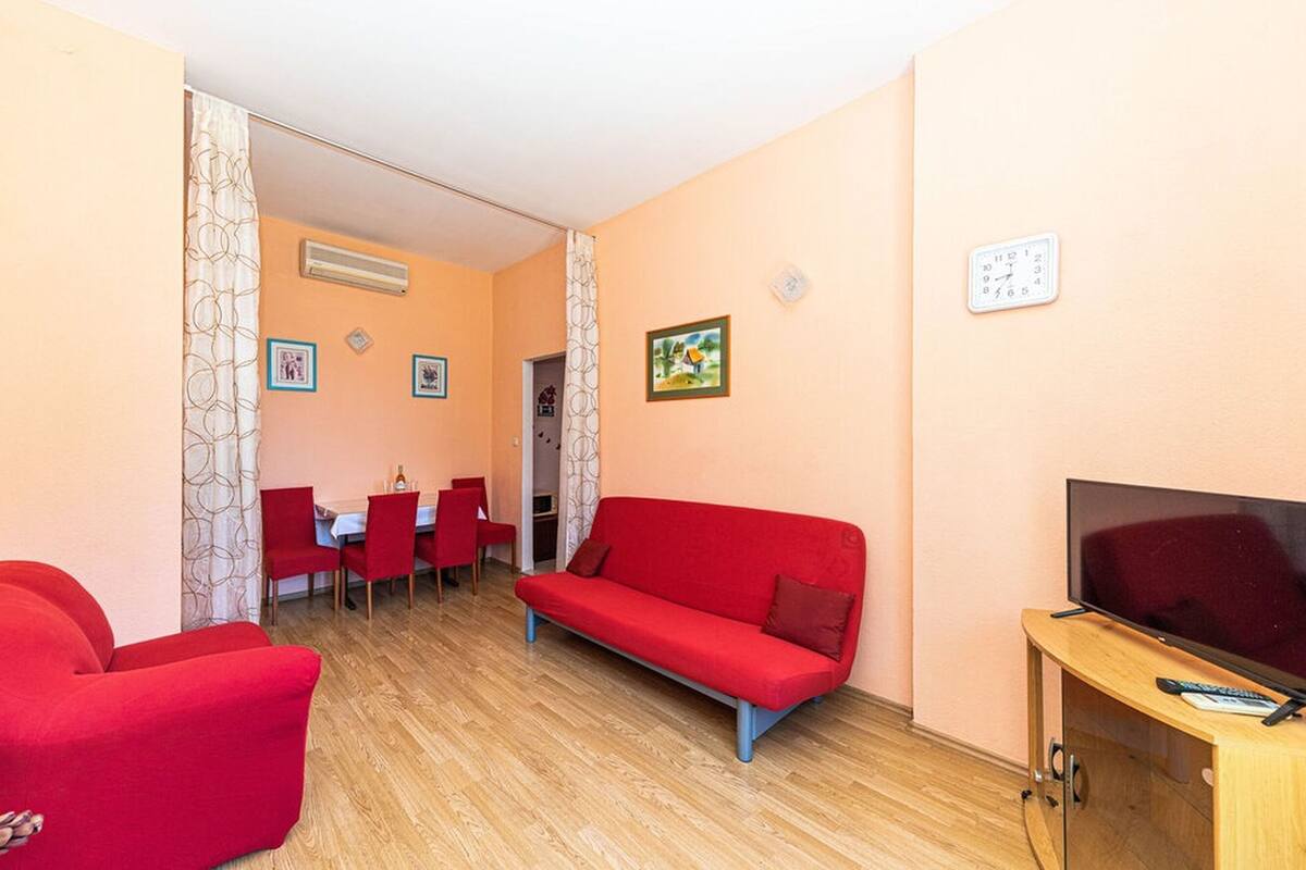 Ein Wohnzimmer mit einem roten Sofa, einem Fernseher und einem Essbereich mit roten Stühlen und einem Tisch.