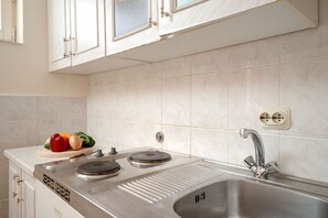 A kitchen with white cabinets, a stainless steel sink, and a cutting board with vegetables. - Apartments Josi (Jelsa)