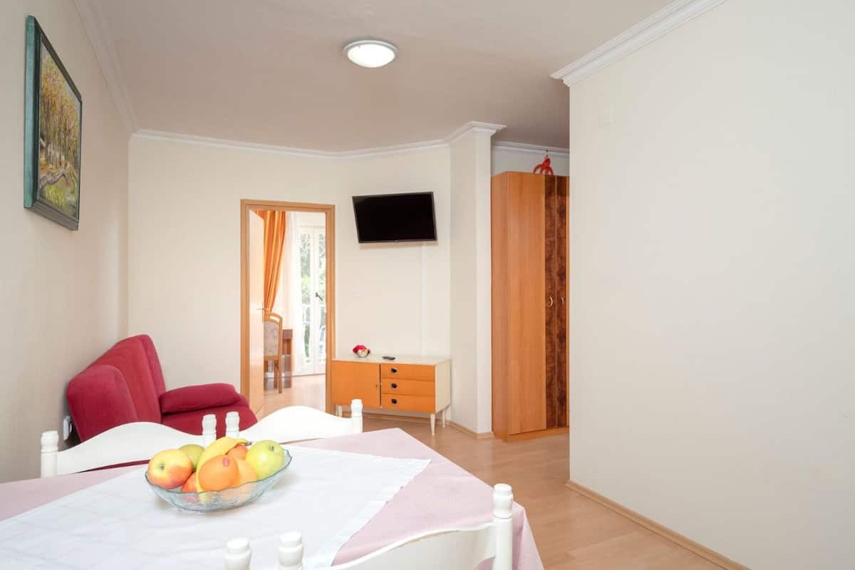 Quarto com cama, mesa de jantar com frutas, televisão, guarda-roupa e porta que dá para o exterior.