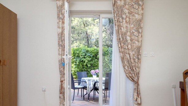 An open door leading to an outdoor patio with a table and chairs, a wooden wardrobe, and a power outlet on the wall. - Apartments Josi (Jelsa)