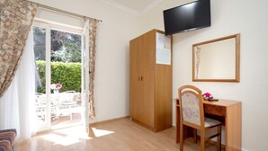 A room with a wooden wardrobe, a desk with a chair, a flat-screen TV mounted on the wall, and a sliding glass door leading to an outdoor seating area. - Apartments Josi (Jelsa)
