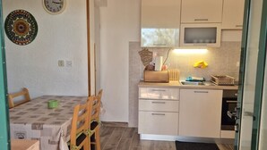 Una cocina compacta con armarios blancos, microondas y una pequeña encimera. Hay una mesa de comedor con sillas y un plato decorativo en la pared.