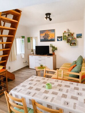 En hyggelig stue med en trætrappe, et fladskærms-tv, en sofa, et spisebord med stole, og en væg pyntet med billeder og små hylder.