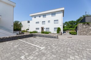A modern building with a flat roof, multiple windows, and a paved courtyard. - Apartments Marina (Malinska-Dubasnica)