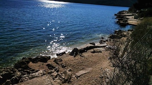Una costa rocciosa con acque limpide che riflettono la luce del sole, circondata da colline.