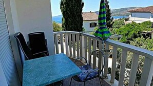 Un balcone con tavolo e sedie, un ombrellone verde e vista sul mare e sulle colline.