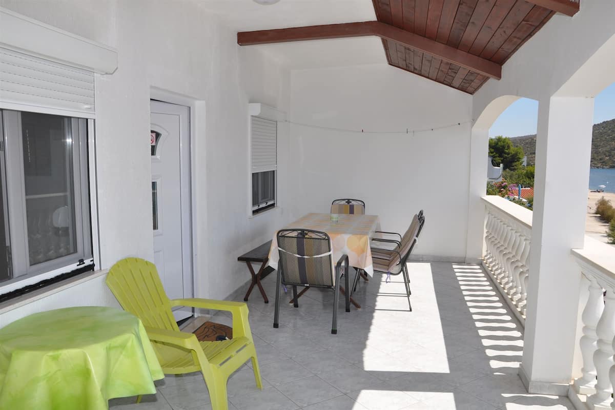 A covered outdoor area with a table and chairs, a window, and a view of the sea.