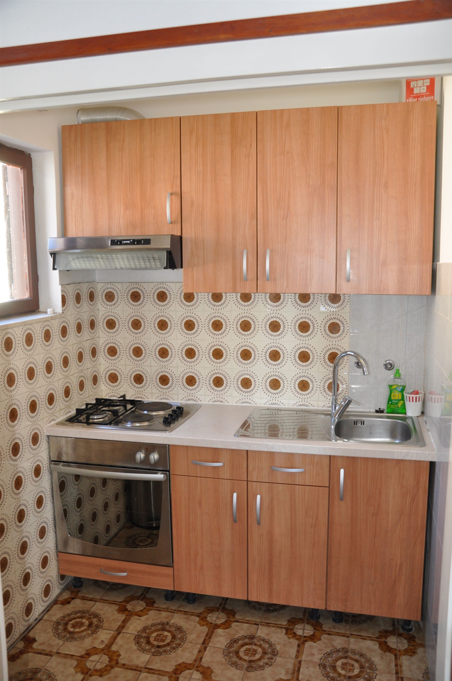 Cocina compacta con armarios de madera, un lavamanos de acero inoxidable y un horno empotrado.