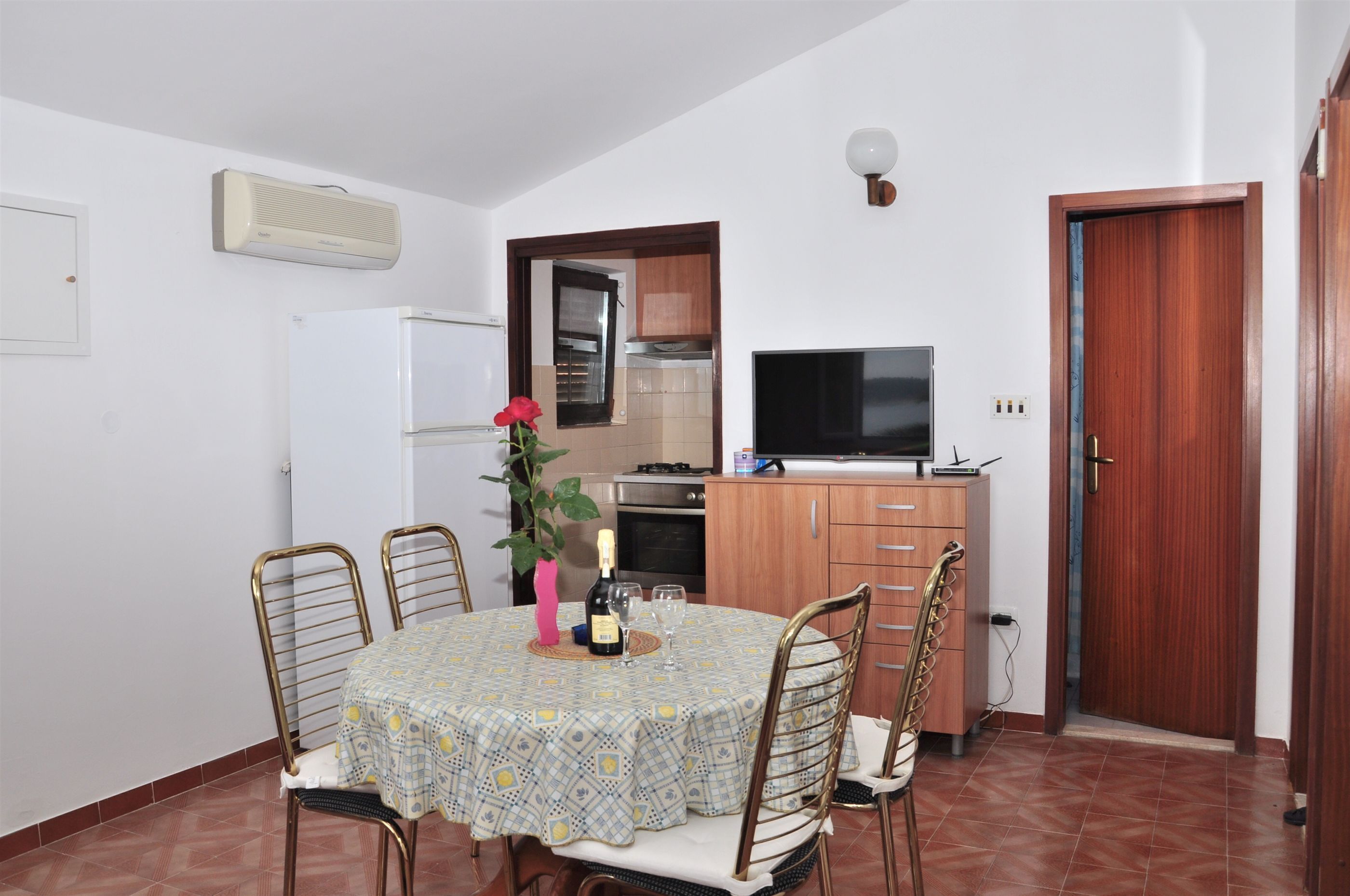 Cucina compatta con frigorifero, fornello e microonde. È presente un tavolo da pranzo con sedie e un televisore su un supporto.