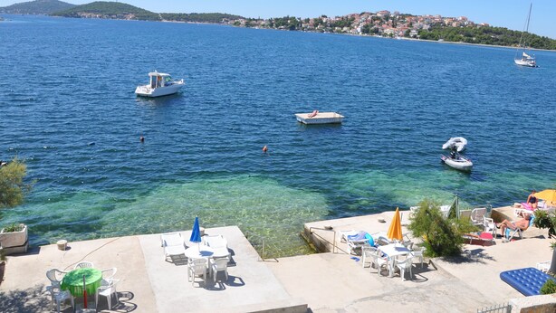 A coastal area with clear blue waters, boats, and a small dock with lounge chairs and umbrellas. - Apartments Bibi (Rogoznica)