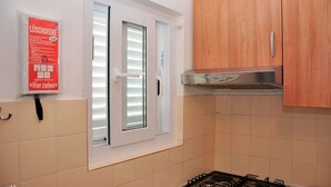 A kitchen with a gas stove, wooden cabinets, and a window with blinds. - Apartments Bibi (Rogoznica)