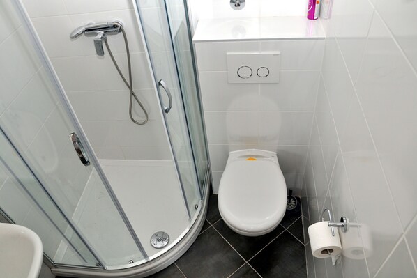 A bathroom with a glass-enclosed shower, a toilet, and a sink. - Apartments Bibi (Rogoznica)