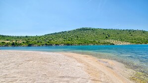 A beach with clear water, a sandy shore, and a hill with greenery in the background. - Apartments Bibi (Rogoznica)