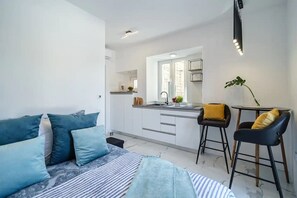 A modern bedroom with a bed, a bedside table, and a small kitchen area with a window, a sink, and a countertop. - Apartment Vin (Supetar)