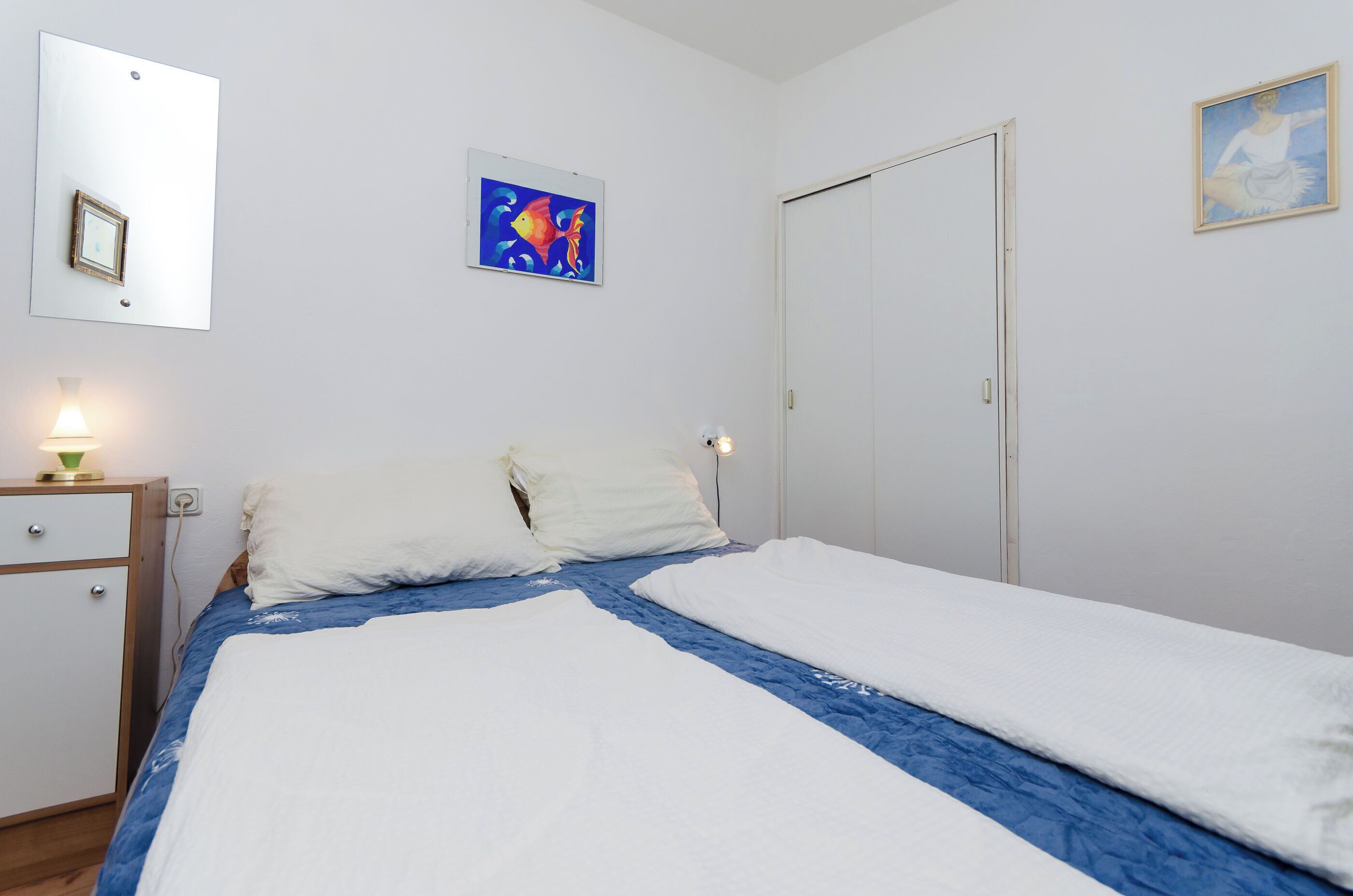 A bedroom with a bed, a nightstand, a dresser, and two paintings on the wall.