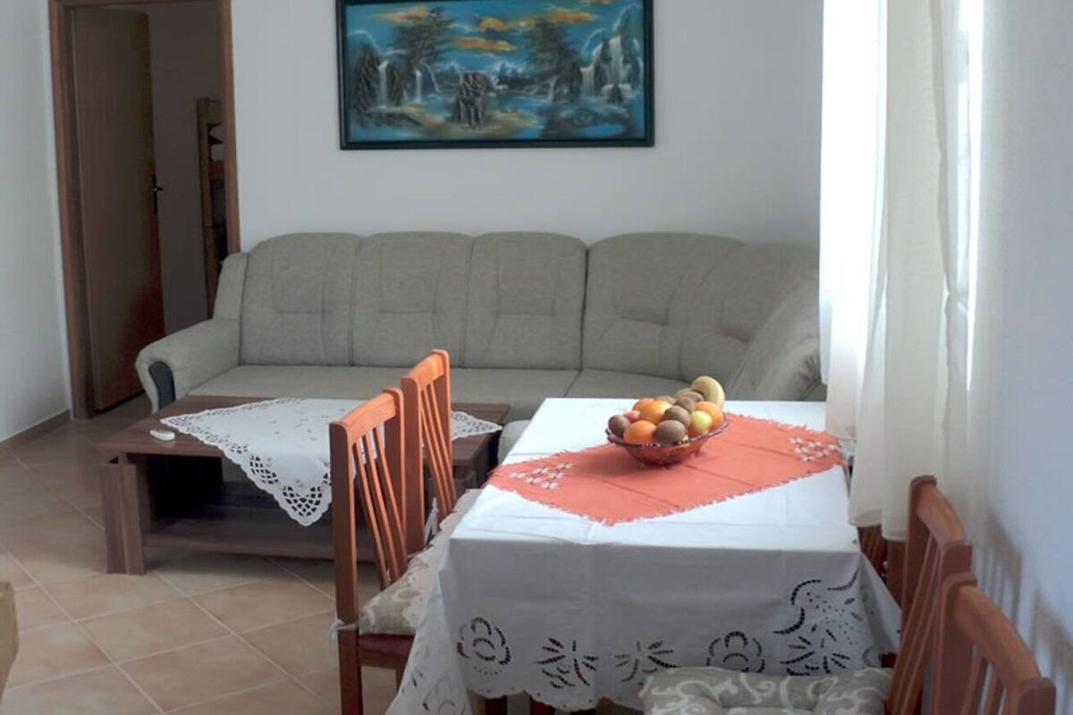 A dining area with a table set for two, a sofa, and a painting on the wall.
