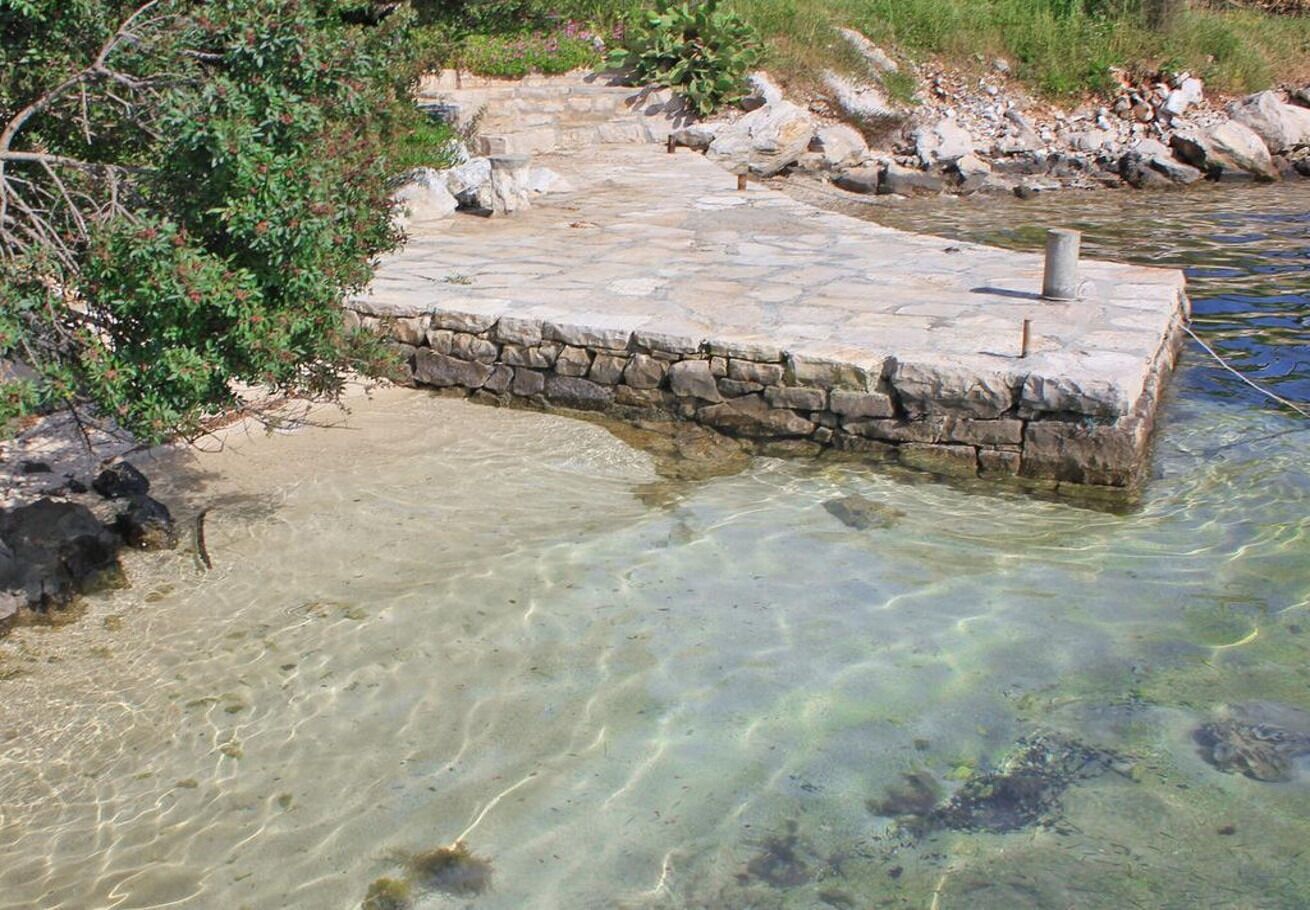 A stone platform extending into clear water, surrounded by rocks and vegetation.