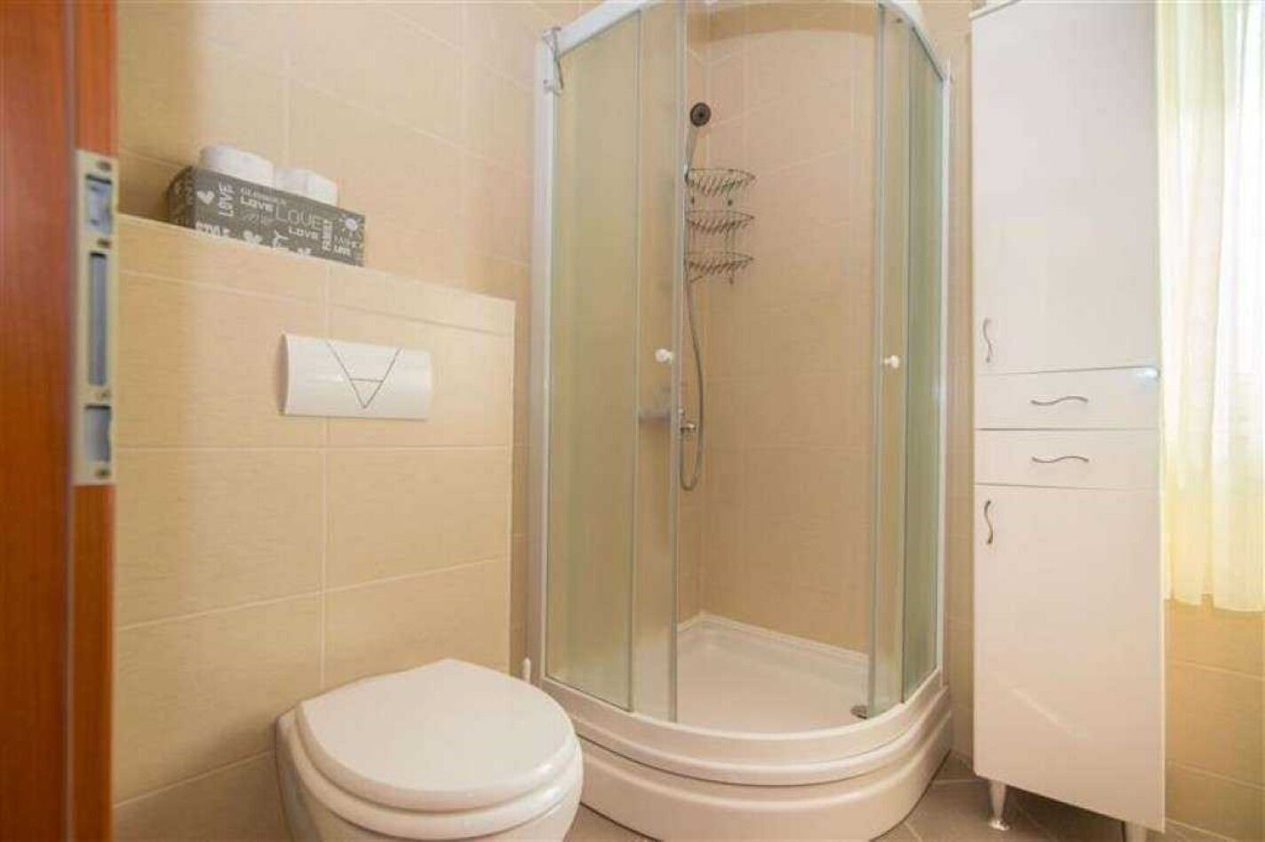 A bathroom with a glass-enclosed shower, a toilet, and a cabinet.