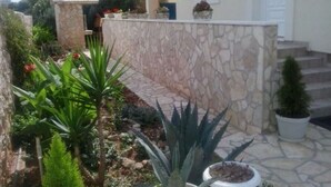 Un espace extérieur entouré de murs en pierre, agrémenté de plantes en pot et d’une petite construction.