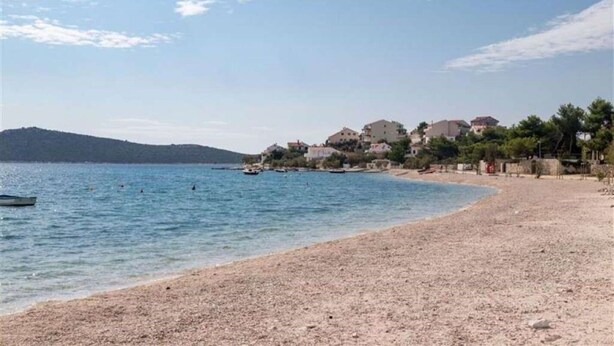 Une plage au rivage de galets, un bateau sur l’eau et des bâtiments en arrière-plan.