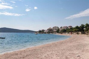 Ein Strand mit Kiesufer, ein Boot im Wasser und Gebäude im Hintergrund.