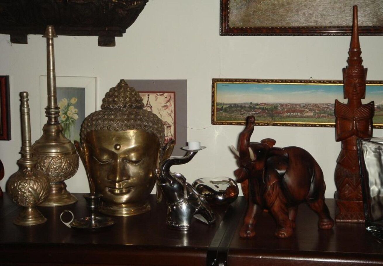 A wooden table with various decorative items including a Buddha statue, an elephant figurine, and a tall, slender object.