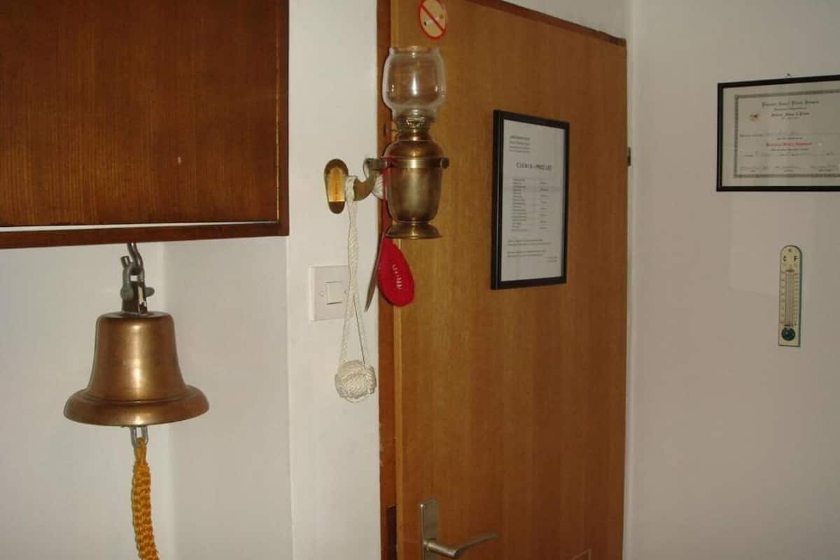 A room with a wooden door, a brass bell, a red telephone, and a framed certificate on the wall.