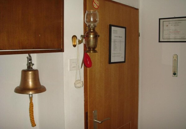 A room with a wooden door, a brass bell, a red telephone, and a framed certificate on the wall. - Rooms Branka (Krizevci)