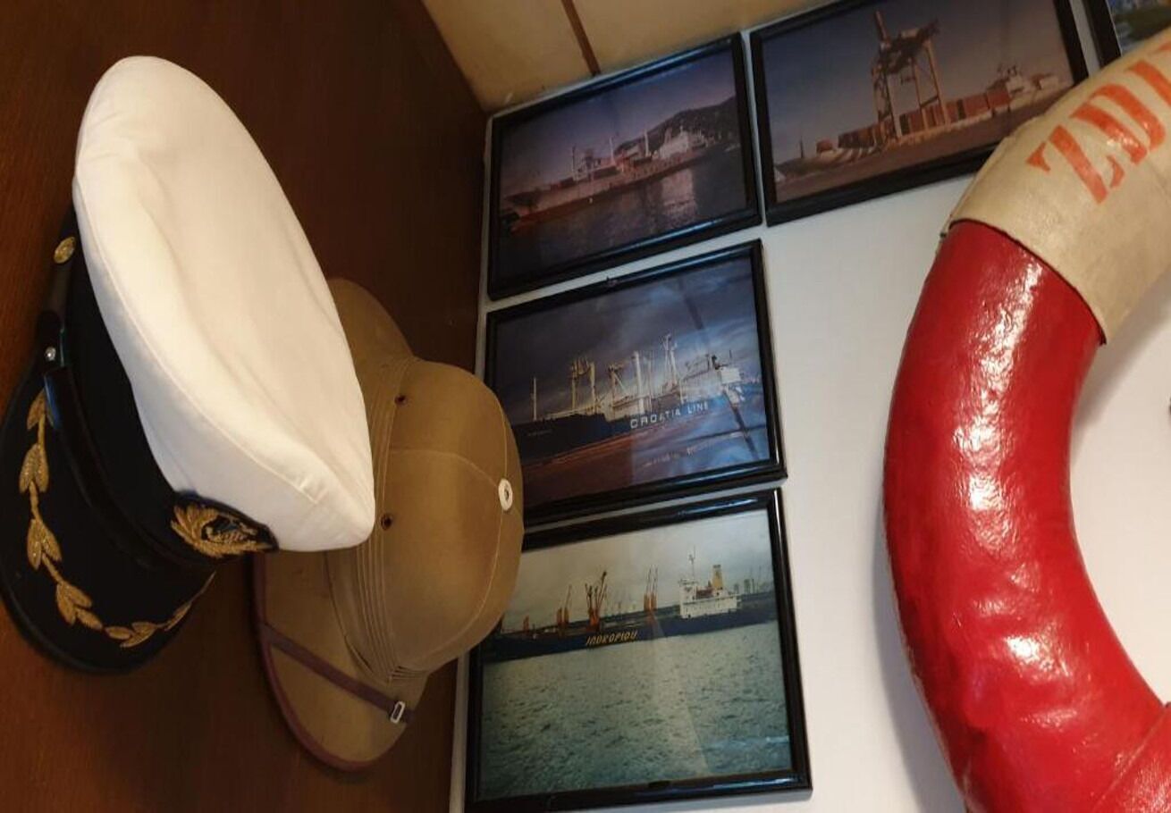 A collection of hats and framed maritime photographs on a wall.