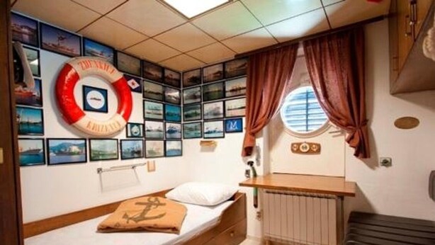 A compact bedroom with a bed, a small desk, a radiator, and a life preserver on the wall. - Rooms Branka (Krizevci)