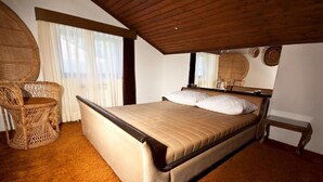 A bedroom with a large bed, a wicker chair, and a wooden ceiling. - Rooms Branka (Krizevci)