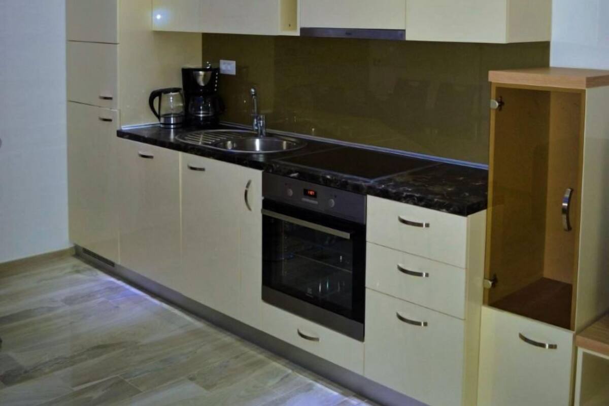 Una cocina moderna con electrodomésticos integrados, armarios de tonos claros y un mueble de madera a la derecha.