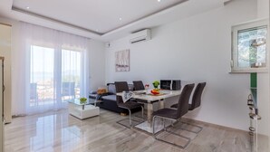 A modern living room with a dining area, large windows, and a view of the outdoors. - Apartments Igor (Kostrena)