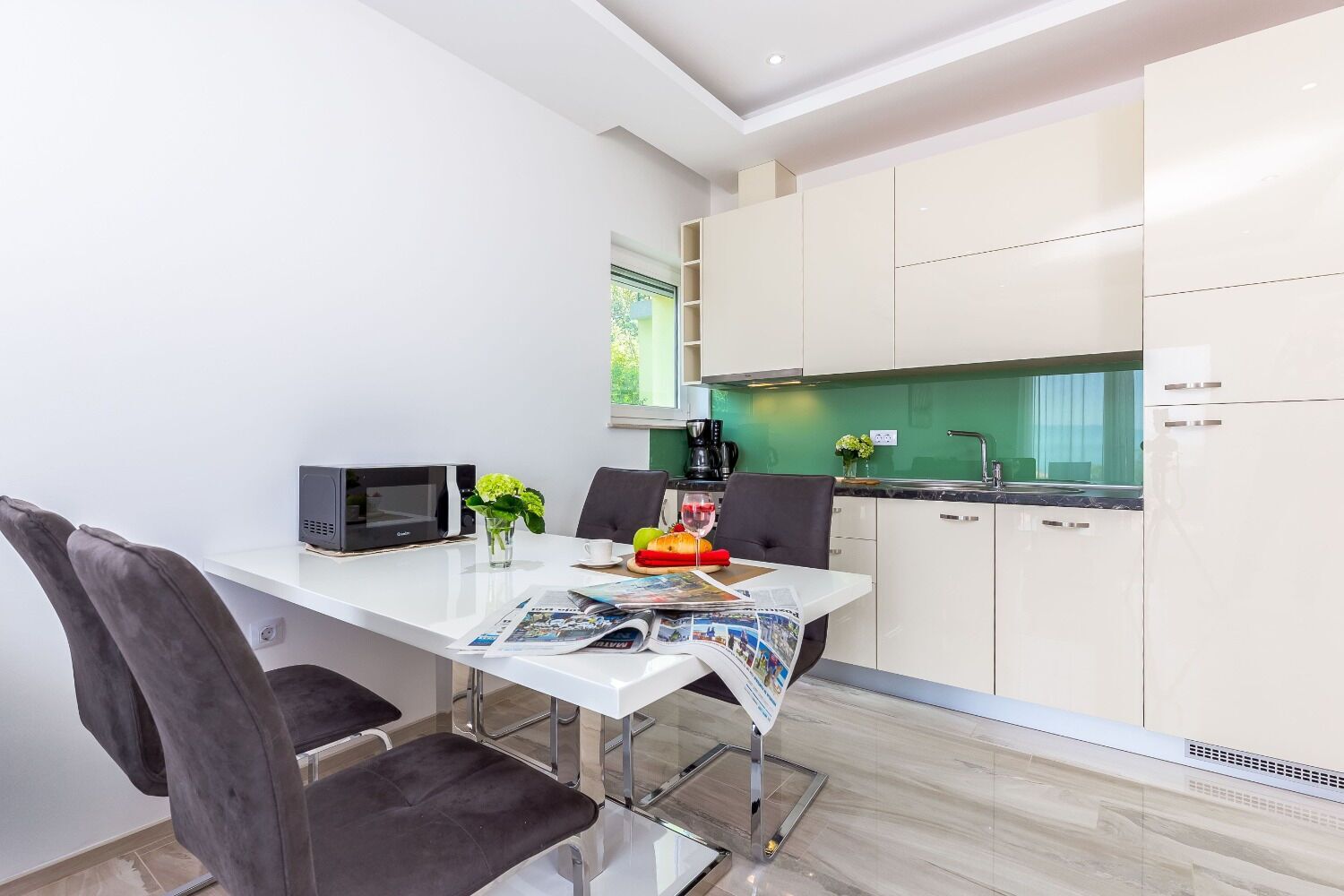 Une cuisine moderne avec des meubles blancs, un micro-ondes noir et un coin repas comprenant une table blanche et deux chaises.