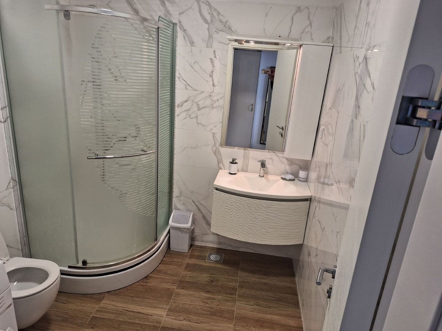 Ein modernes Badezimmer mit einer gläsernen Duschkabine, einem weißen Waschbecken mit Marmorplatte und einer Toilette.