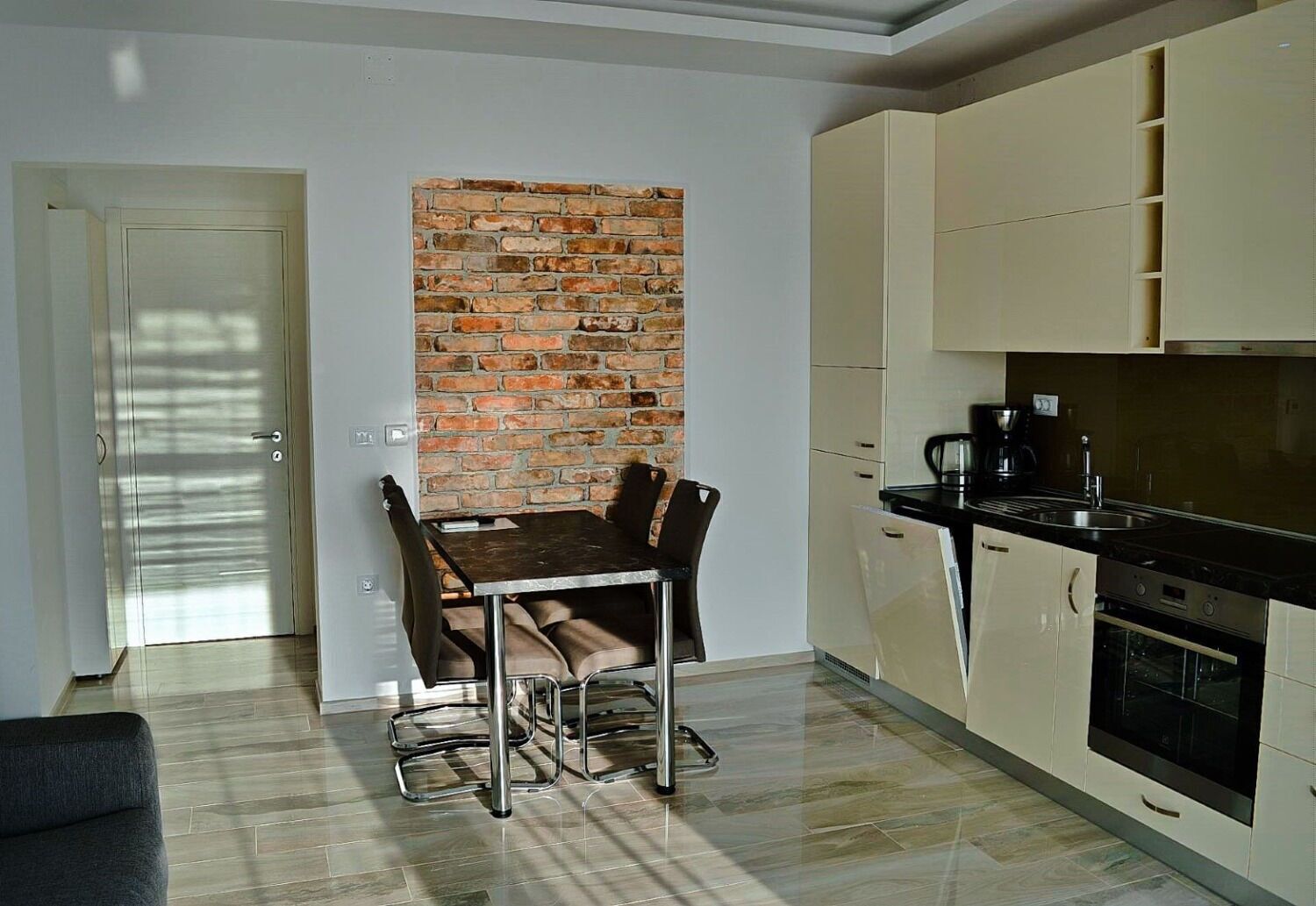 A modern kitchen with a brick accent wall, a dining area with a table and chairs, and a separate dining room with a sofa.