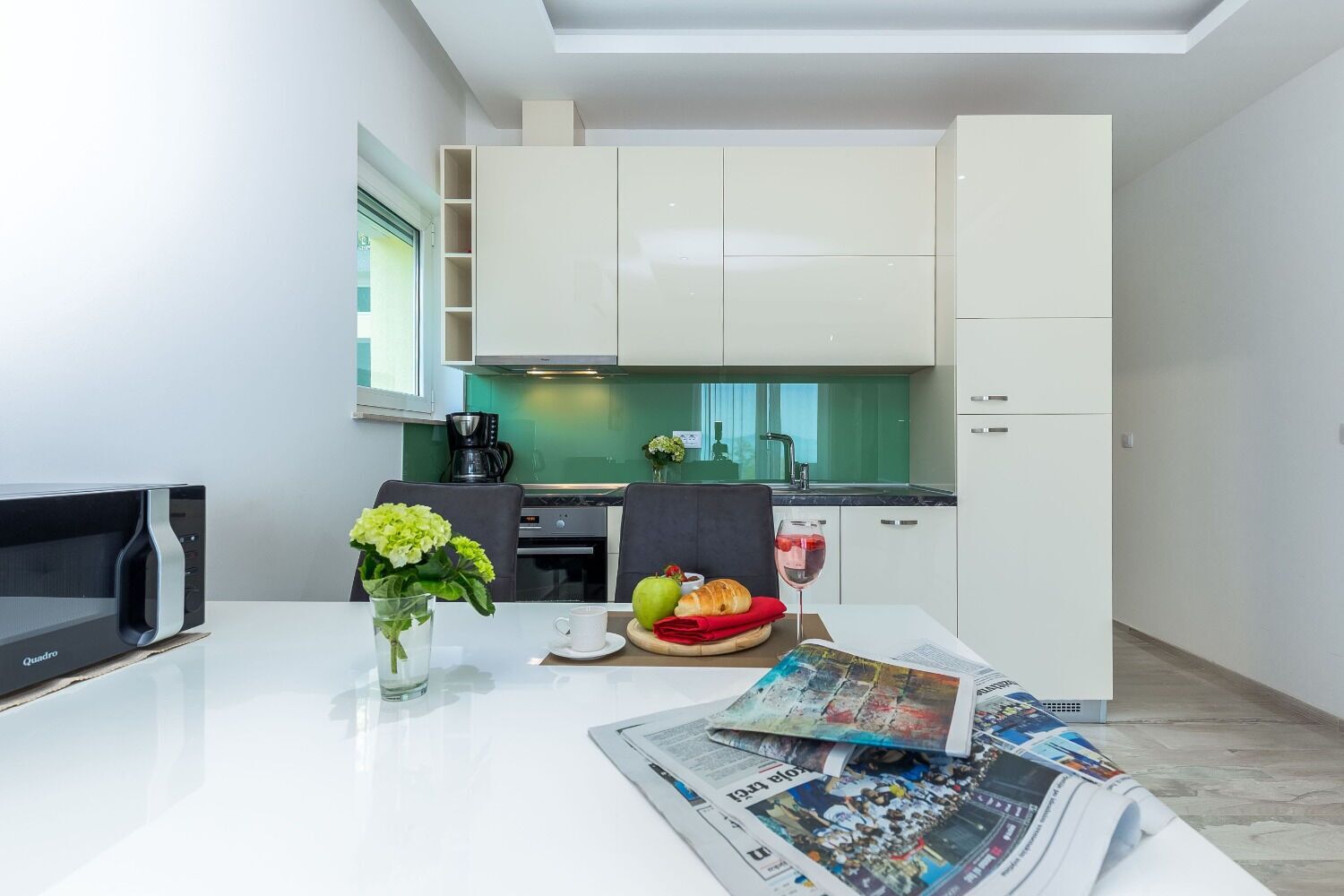 A modern kitchen with white cabinets, a dining table with a vase of flowers, and a breakfast setting.