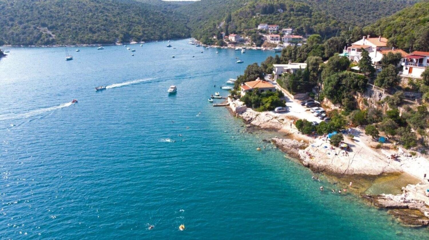 Una zona costera con barcos en el agua, una playa rocosa y edificios en la colina.
