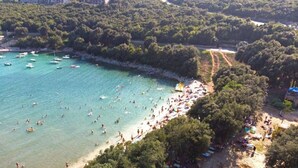 Luchtbeeld van een strand met boten, mensen en bomen.