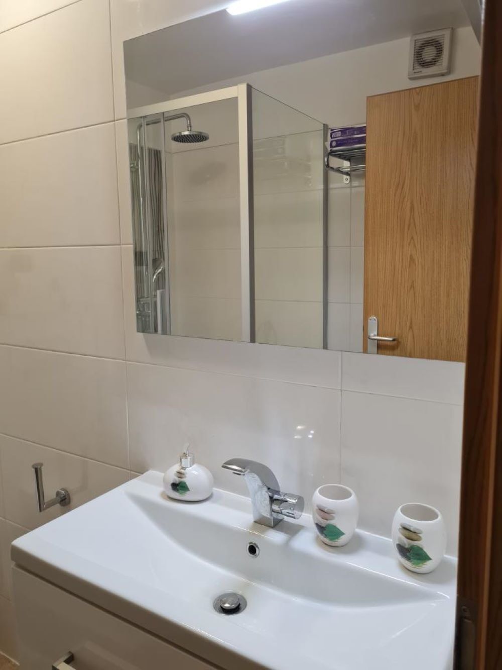A bathroom with a white sink, a mirror, a shower, and a wooden cabinet.