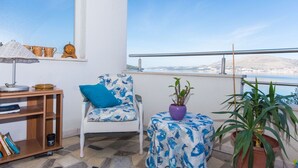 A balcony with a white chair, a small table, a lamp, and potted plants. - Apartments Duga (Okrug)