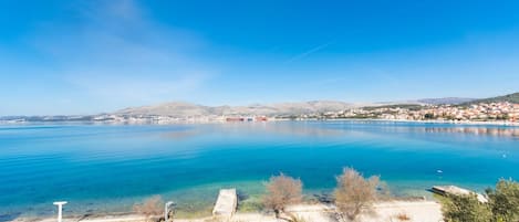 A coastal view with a clear blue sea, a sandy beach, and a distant town.