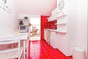 A compact kitchen with white cabinetry, a red-tiled floor, and a dining area with a white table and chairs. - House Katy (Posedarje)