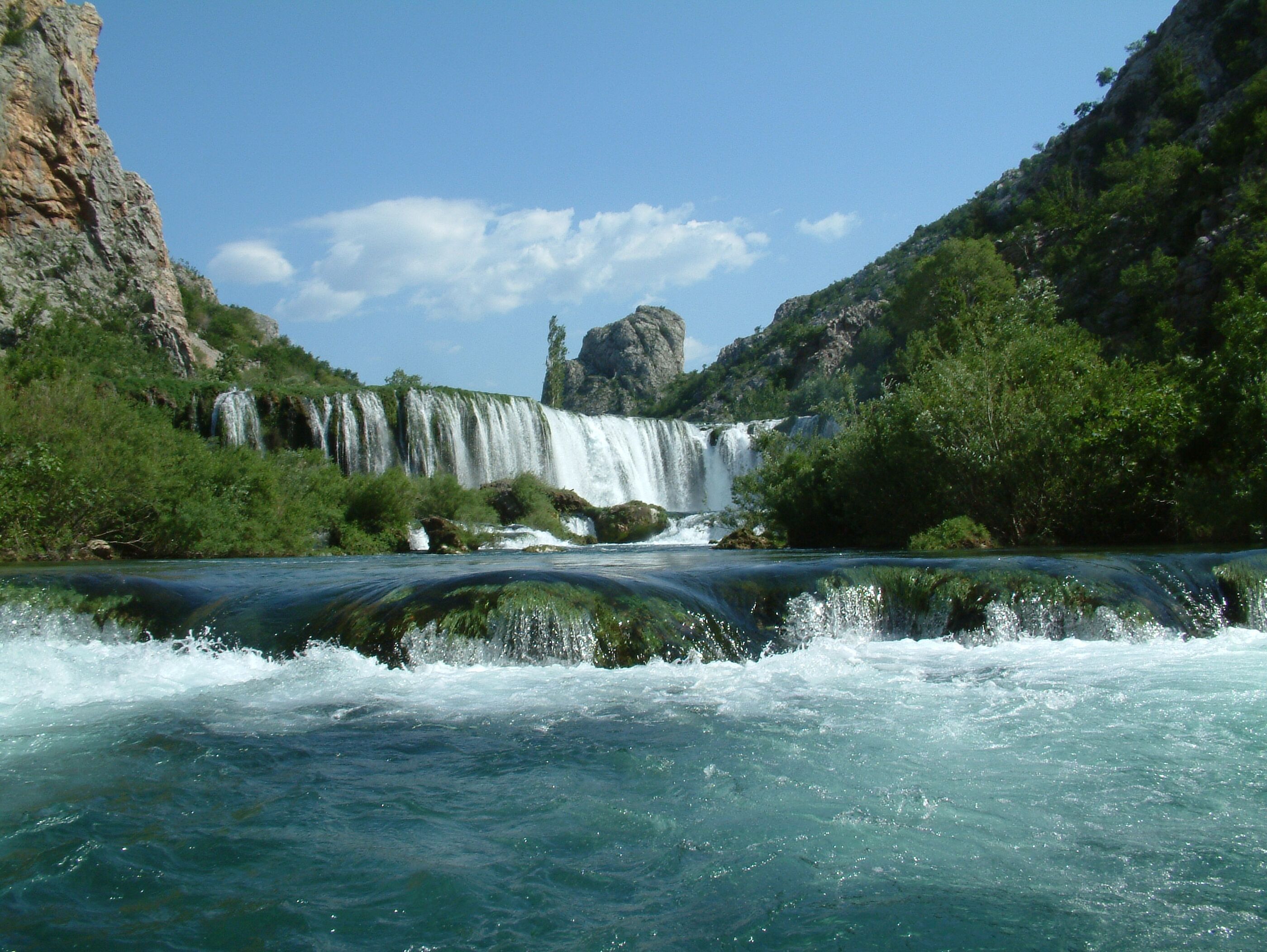 Une rivière avec une cascade et une végétation luxuriante tout autour.